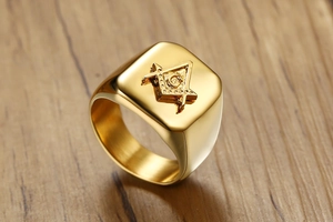 Macro detail of gold Freemason signet ring with engraved G symbol on wooden surface