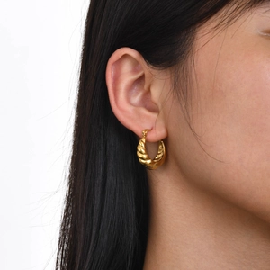 Détail des boucles d'oreilles créoles torsadées en acier doré portées sur l'oreille