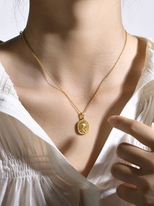 Dettaglio di una collana dorata con pendente ovale a rilievo di rosa indossata da modella