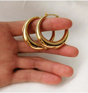Gros plan de boucles d'oreilles créoles dorées épaisses montrant la texture polie 18K