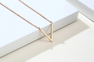 Gros plan du collier avec pendentif en V or rose sur un support géométrique blanc pur