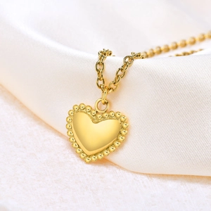 Gold-plated stainless steel heart pendant necklace with beaded edges on satin background