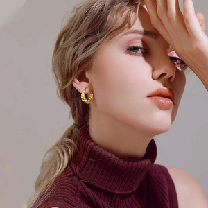 Détail des boucles d'oreilles créoles torsadées dorées portées par un mannequin chic