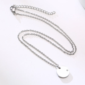 Detailed close-up of a silver minimalist round disc pendant with small zircon gemstone