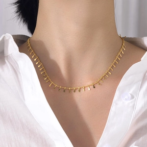 Détail du collier à pampilles dorées en acier inoxydable sur chemise blanche