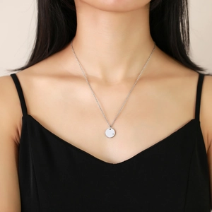 Close-up of a minimalist silver necklace with a round pendant and a small cubic zirconia