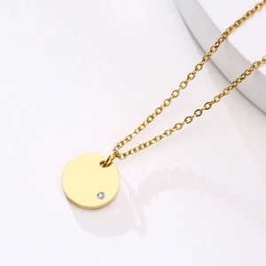 Close-up of golden stainless steel round pendant with a single zircon on white background