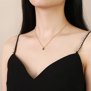 Detail of emerald green rectangular pendant necklace on a gold chain worn by a model