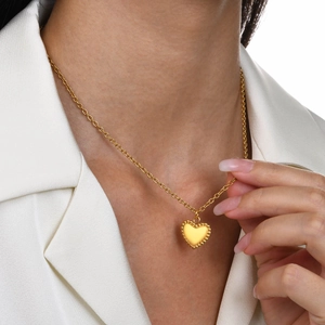 Detail of gold heart pendant necklace with beaded edges worn on a white suit