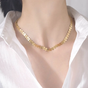 Gros plan du collier doré en acier inoxydable à maillons cœurs sur une chemise blanche