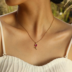 Gros plan du pendentif tulipe dorée avec zircon rouge sur une chaîne délicate