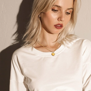 Detail of a golden heart pendant necklace with beaded edges worn on a model collarbone