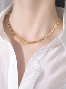 Gros plan d'un collier à maillons en forme de cœur doré porté sur un chemisier blanc