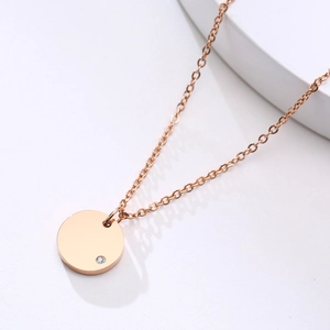 Detail of rose gold round pendant necklace with small cubic zirconia on a white surface