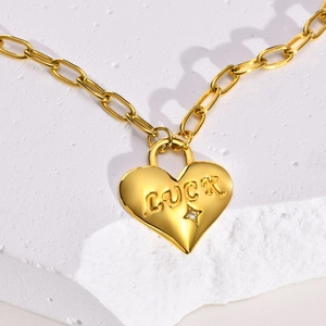 Detail of gold heart pendant with LUCK engraving and zircon on a paperclip chain