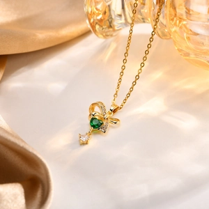 Dettaglio di una collana a fiocco dorata con gemma verde a cuore e zircone trasparente