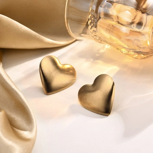 Nahaufnahme von 18K Gold Herzohrringen mit gebürstetem Metall-Finish auf Satinhintergrund