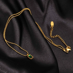 Golden bead necklace with emerald green rectangular pendant on black silk background