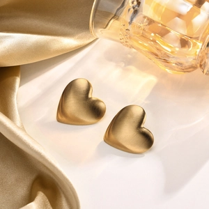 Detail von gebürsteten 18K Gold Herzohrringen auf Seidenhintergrund mit Makro-Textur