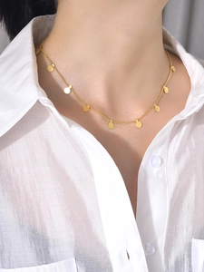 Détail d'un collier minimaliste en acier doré avec de petits charms ronds polis