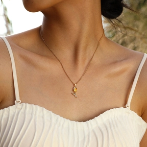 Gros plan du collier pendentif tulipe dorée avec zircon rouge porté par un mannequin