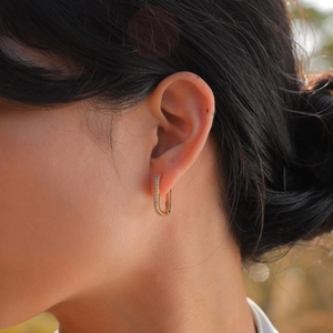 Close-up of elegant U-shaped gold earrings with zircon crystals worn on ear