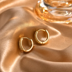 Detailed close-up of 18K gold huggie earrings with micro-pave zircons on silk fabric