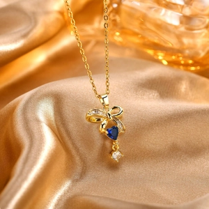 Dettaglio del ciondolo a fiocco dorato con zircone blu a cuore su sfondo di seta