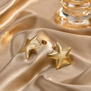 Nahaufnahme matter 18K Gold Stern-Ohrstecker auf elegantem champagnerfarbenem Seidenstoff