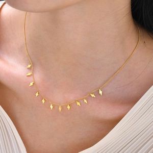 Detailansicht einer goldenen Halskette mit kleinen Blitz-Anhängern am Hals des Models