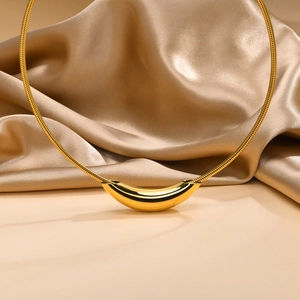 Close-up of polished gold stainless steel curved tube pendant on a snake chain collar