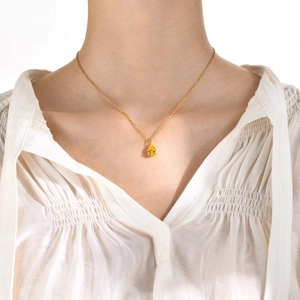 Gros plan d'un collier chaîne O dorée orné d'un zircon jaune étincelant en forme de poire