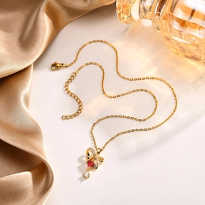Dettaglio della collana a fiocco dorato con cuore rosso su tessuto di raso champagne