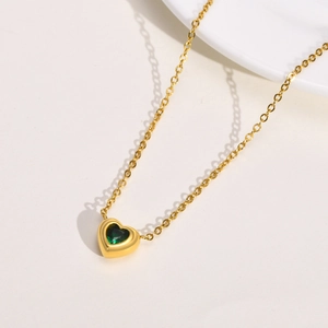 Detail of a gold heart necklace with a vibrant green zircon stone on a white background