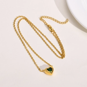 Detail of gold heart pendant necklace featuring a deep green zircon stone and cable chain