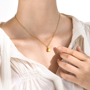 Détail d'un pendentif en pierre jaune poire sur une chaîne en or portée par un mannequin