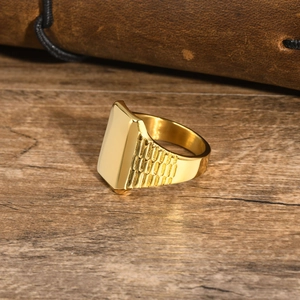 Dettaglio anello a sigillo dorato in acciaio con trama laterale su tavolo di legno