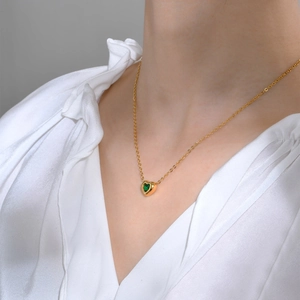 Close-up of golden heart pendant necklace with green zircon on a model wearing white silk