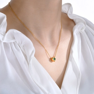 Elegant gold heart pendant necklace with green gemstone worn by model on white shirt