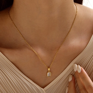Close-up of a gold necklace with a rectangular mother-of-pearl pendant on a model