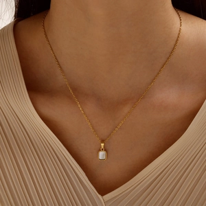 Detail of a gold thin chain necklace with a square white mother of pearl pendant on a neck