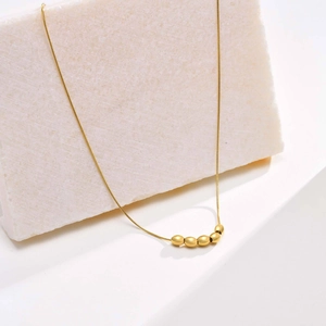 Detailed view of minimalist gold snake chain necklace with five polished metallic beads