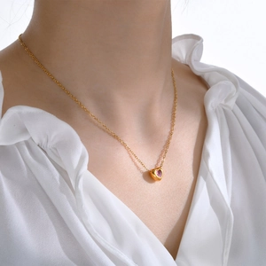 Close-up of a gold heart pendant necklace with pink zircon on a model's neck