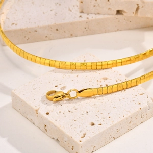 Detailed macro view of gold hammered flat snake chain necklace on beige stone pedestal