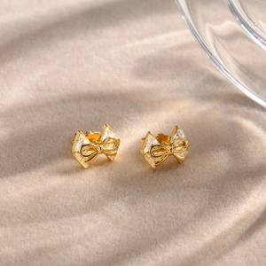 Boucles d'oreilles nœud dorées avec cristaux de zircon sur fond minimaliste chic