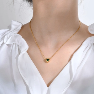 Detail of a gold heart pendant necklace with green gemstone on a female model neck