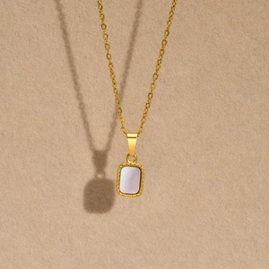 Close-up of golden rectangular mother of pearl pendant with milgrain edge and fine chain