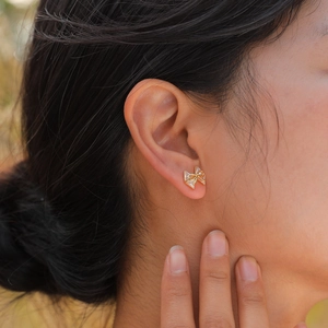 Boucles d'oreilles nœud dorées avec zircons étincelants portées par un mannequin