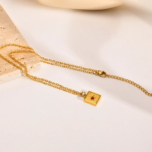 Détail du pendentif carré doré avec étoile et pierre rouge sur une chaîne délicate