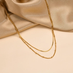 Double-layered gold stainless steel necklace with bead and snake chain on silk background